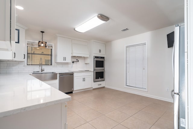 kitchen with light stone counters, hanging light fixtures, white cabinets, appliances with stainless steel finishes, and sink