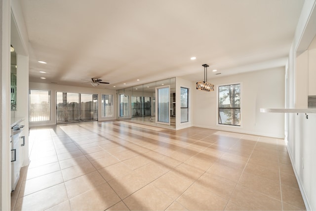 spare room with a healthy amount of sunlight, light tile patterned flooring, and ceiling fan with notable chandelier