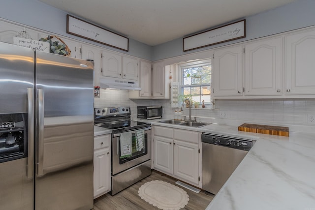 kitchen with sink, white cabinets, hardwood / wood-style floors, light stone countertops, and appliances with stainless steel finishes