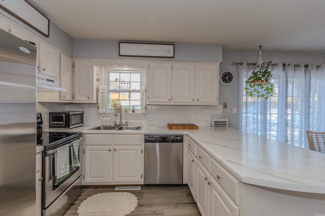 kitchen featuring white cabinets, stainless steel appliances, kitchen peninsula, sink, and range hood