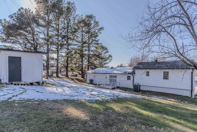 snow covered rear of property with a yard, central AC, and a storage unit