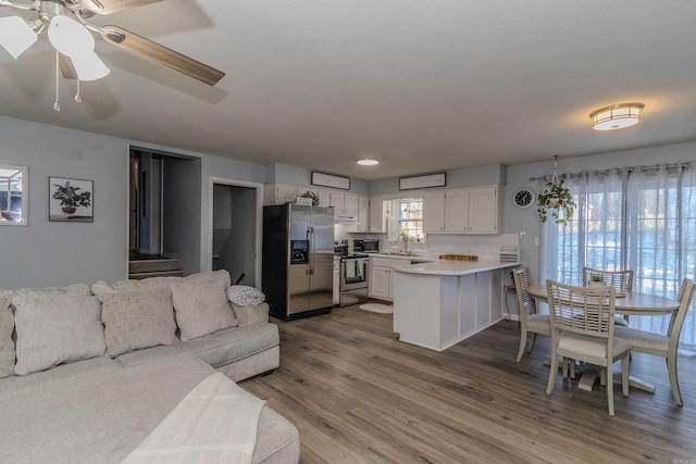 kitchen featuring stainless steel appliances, white cabinetry, tasteful backsplash, hardwood / wood-style flooring, and kitchen peninsula