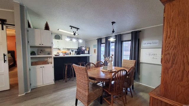 dining room with hardwood / wood-style flooring, a textured ceiling, a barn door, and ornamental molding