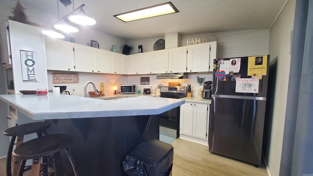 kitchen with fridge, white cabinets, stainless steel electric range oven, a breakfast bar area, and hanging light fixtures