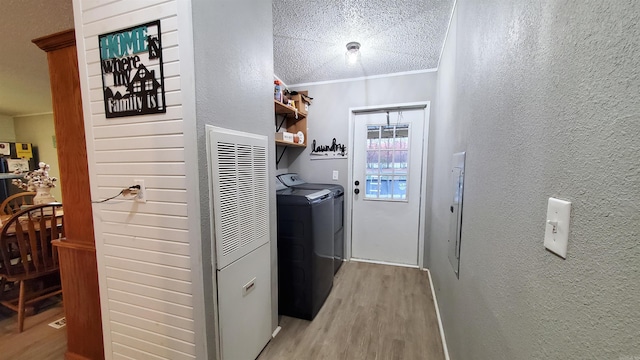 laundry room featuring light hardwood / wood-style floors, a textured ceiling, separate washer and dryer, and crown molding