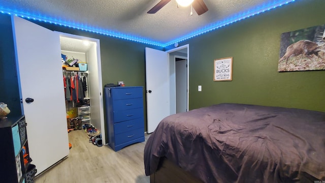 bedroom featuring a textured ceiling, ceiling fan, light wood-type flooring, a closet, and a walk in closet