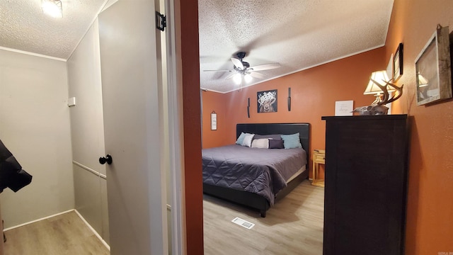 bedroom featuring ceiling fan, light hardwood / wood-style flooring, ornamental molding, and a textured ceiling