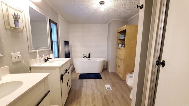 bathroom with toilet, a bathing tub, vanity, hardwood / wood-style flooring, and a textured ceiling