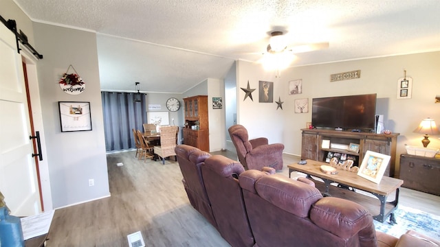 living room featuring a textured ceiling, lofted ceiling, light wood-type flooring, a barn door, and ceiling fan