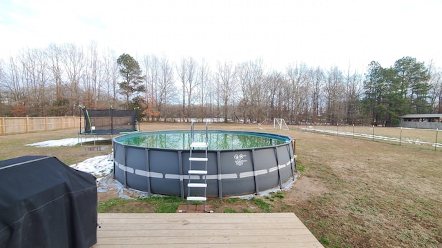 view of swimming pool featuring grilling area, a trampoline, and a wooden deck