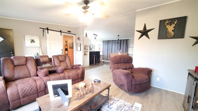 living room with a textured ceiling, light hardwood / wood-style flooring, a barn door, crown molding, and ceiling fan