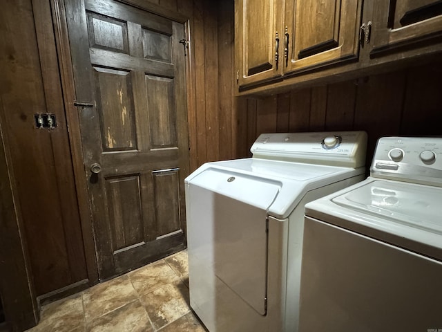 clothes washing area with wooden walls, washing machine and clothes dryer, and cabinets