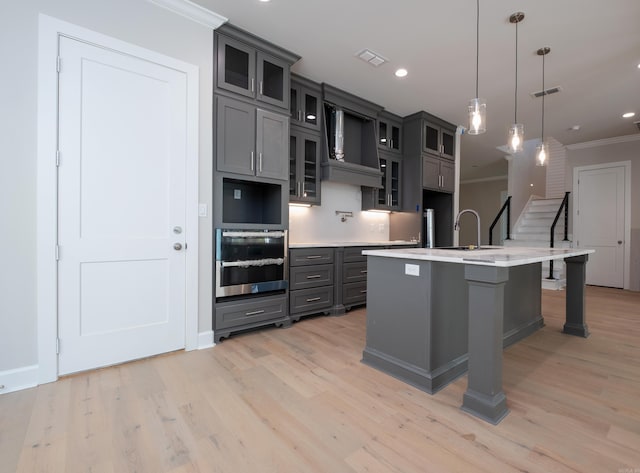 kitchen with pendant lighting, oven, an island with sink, and gray cabinetry