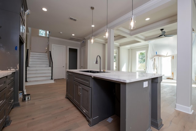 kitchen with sink, ornamental molding, ceiling fan, light stone countertops, and a center island with sink