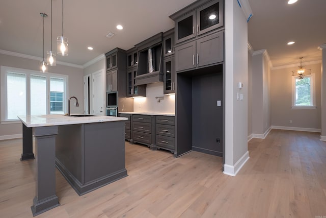 kitchen with an island with sink, pendant lighting, premium range hood, and sink