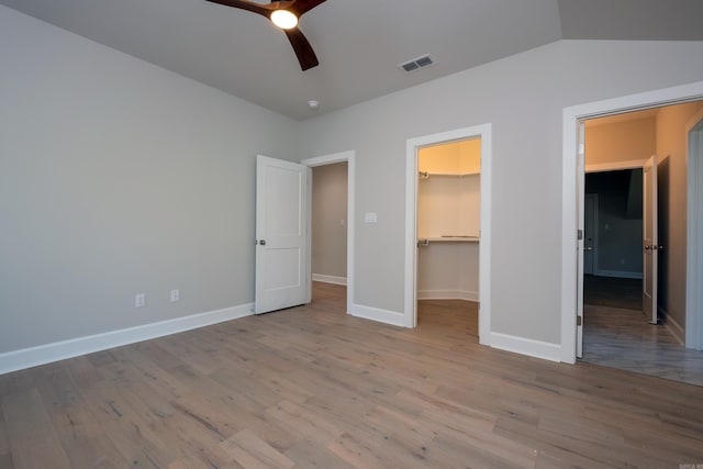 unfurnished bedroom with ceiling fan, a walk in closet, light hardwood / wood-style floors, and a closet