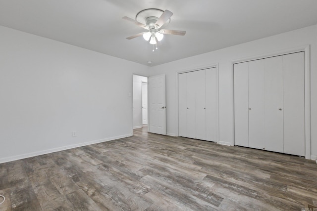 unfurnished bedroom with ceiling fan, hardwood / wood-style floors, and multiple closets