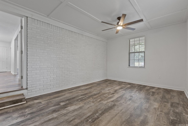 unfurnished room with ceiling fan, dark hardwood / wood-style floors, coffered ceiling, and brick wall