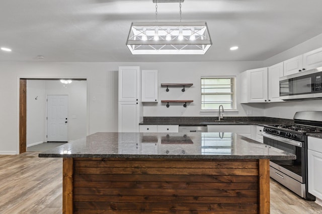 kitchen featuring hanging light fixtures, stainless steel appliances, a kitchen island, dark stone countertops, and sink