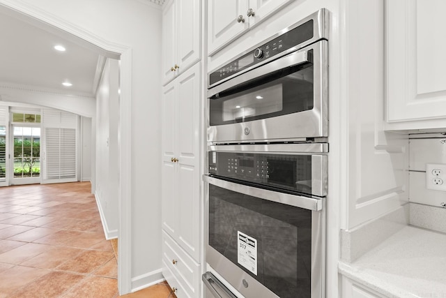 kitchen featuring double oven, white cabinetry, ornamental molding, and light tile patterned flooring