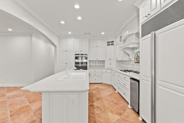 kitchen with paneled built in fridge, a kitchen island with sink, white cabinetry, double oven, and sink