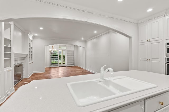 kitchen featuring a brick fireplace, crown molding, white cabinets, light tile patterned flooring, and sink