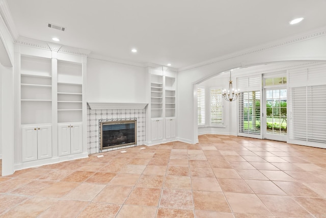 unfurnished living room with an inviting chandelier, a tiled fireplace, ornamental molding, light tile patterned floors, and built in shelves