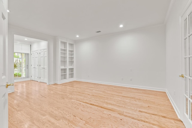 empty room with crown molding, built in features, and light hardwood / wood-style flooring