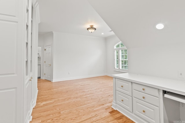 interior space with built in desk, ornamental molding, and light wood-type flooring