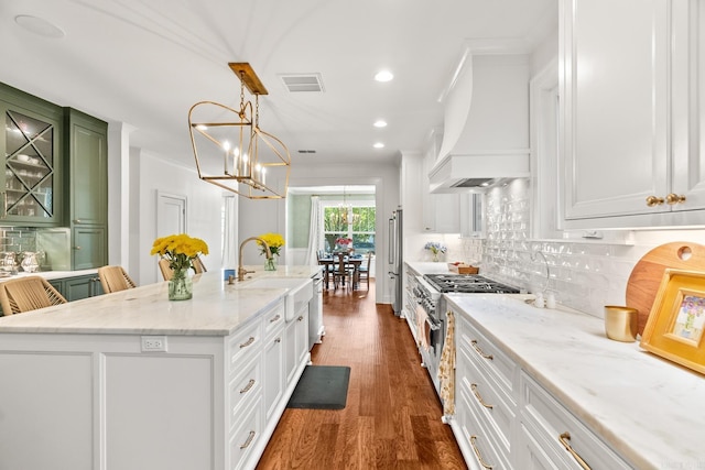 kitchen with a kitchen island with sink, custom range hood, pendant lighting, high end stove, and white cabinets