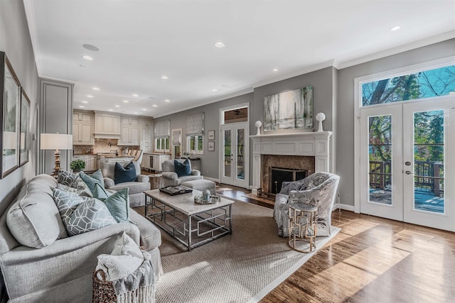 living room featuring french doors, a premium fireplace, wood-type flooring, and crown molding