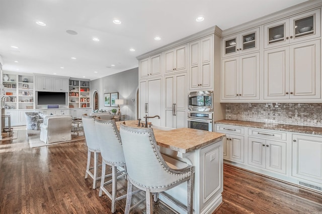 kitchen with a kitchen breakfast bar, stainless steel appliances, an island with sink, dark hardwood / wood-style floors, and decorative backsplash