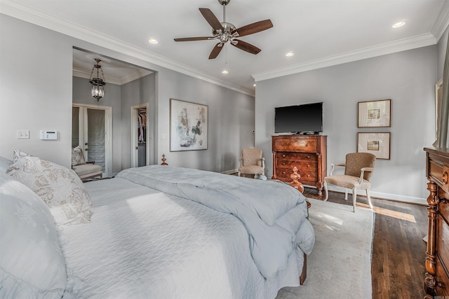 bedroom with dark wood-type flooring, a closet, crown molding, ceiling fan with notable chandelier, and a walk in closet