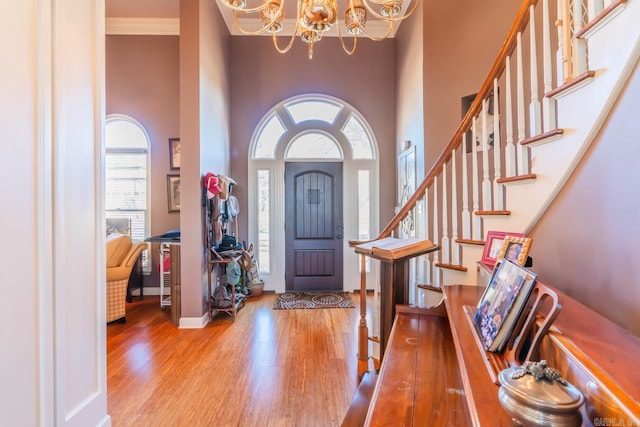 foyer featuring a towering ceiling, ornamental molding, a notable chandelier, and light hardwood / wood-style flooring