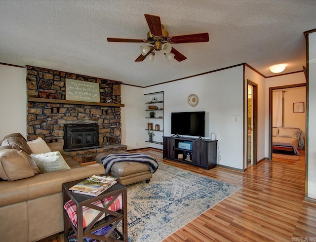 living room with ceiling fan, ornamental molding, a wood stove, a textured ceiling, and light hardwood / wood-style flooring