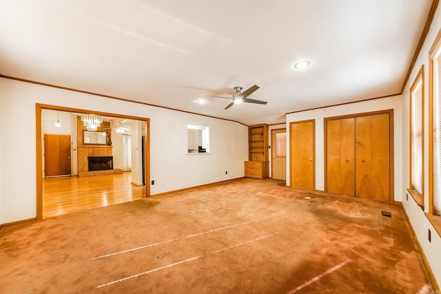 unfurnished bedroom featuring multiple closets, carpet flooring, ceiling fan with notable chandelier, a fireplace, and ornamental molding