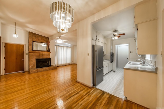 kitchen with vaulted ceiling, stainless steel fridge, ceiling fan with notable chandelier, a fireplace, and sink