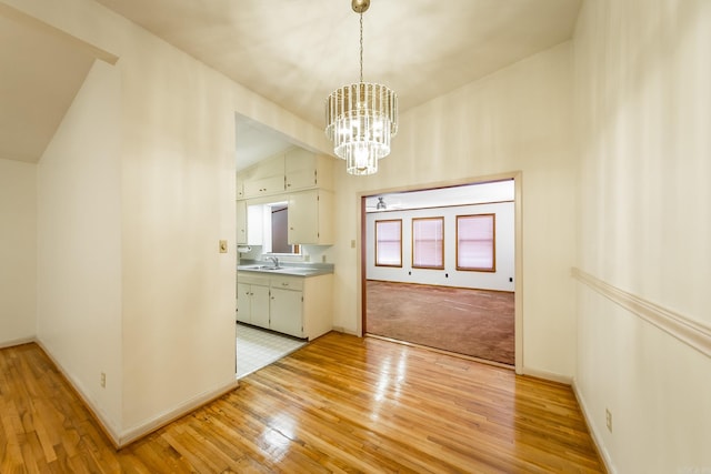 unfurnished dining area featuring lofted ceiling, an inviting chandelier, sink, and light hardwood / wood-style flooring