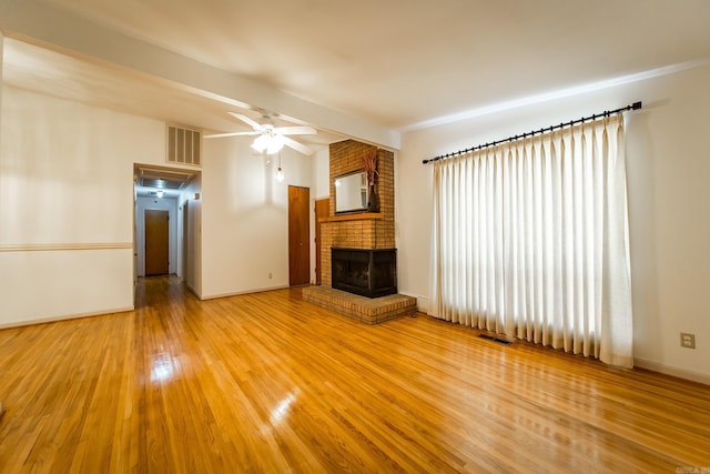 unfurnished living room with ceiling fan, a brick fireplace, beam ceiling, and hardwood / wood-style flooring