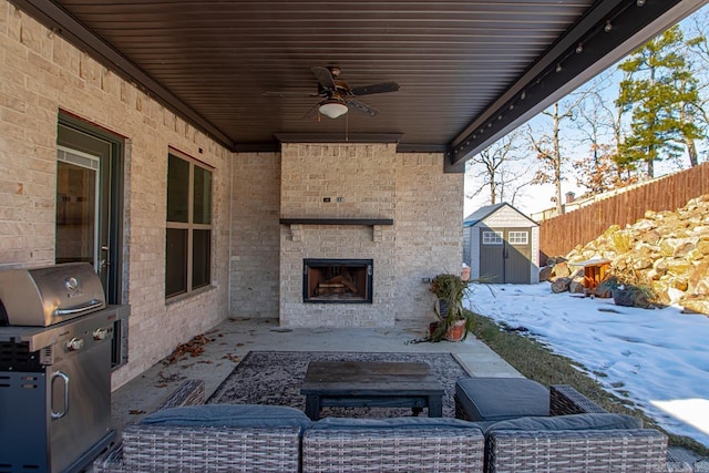 snow covered patio featuring a storage unit, ceiling fan, and an outdoor brick fireplace