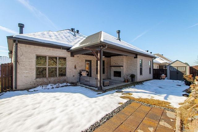 snow covered house featuring a fireplace, a storage shed, and a patio