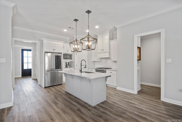 kitchen with appliances with stainless steel finishes, pendant lighting, an island with sink, and white cabinetry