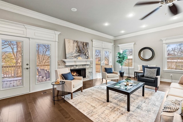 living room with ornamental molding, dark hardwood / wood-style flooring, a stone fireplace, and ceiling fan