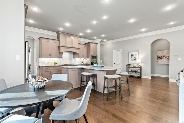 kitchen featuring stainless steel appliances, a kitchen bar, tasteful backsplash, an island with sink, and light stone countertops