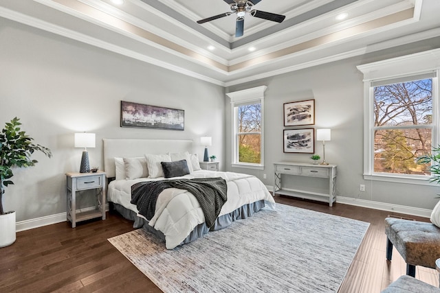 bedroom featuring ceiling fan, a tray ceiling, ornamental molding, and dark wood-type flooring