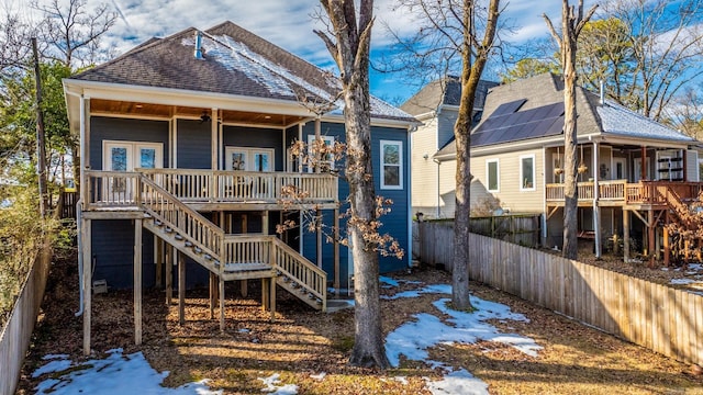 snow covered rear of property with solar panels, french doors, and a wooden deck