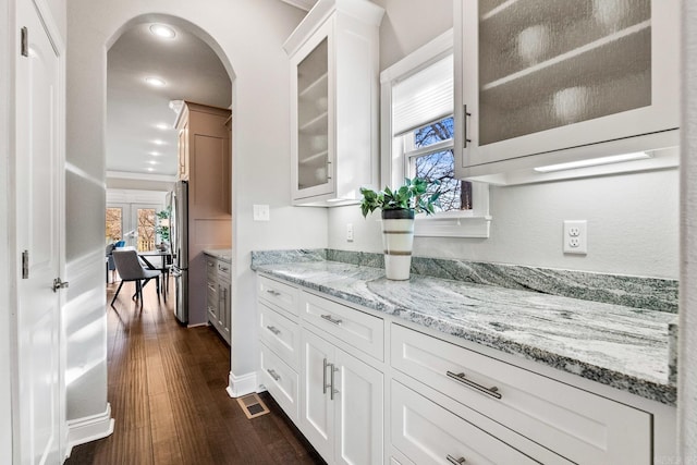 kitchen with white cabinetry, light stone counters, stainless steel refrigerator, crown molding, and dark wood-type flooring