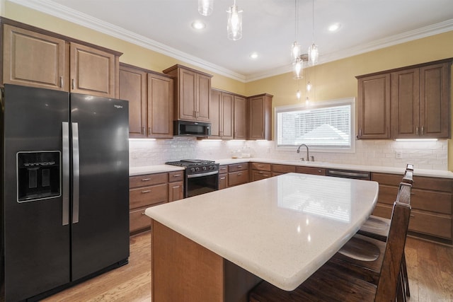 kitchen with sink, hanging light fixtures, a kitchen island, black appliances, and a kitchen bar