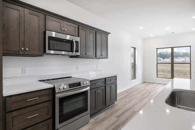 kitchen featuring light stone countertops, light wood-type flooring, dark brown cabinets, and appliances with stainless steel finishes