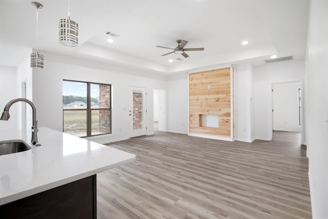 unfurnished living room with sink, ceiling fan, light hardwood / wood-style flooring, and a raised ceiling